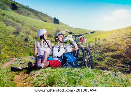 Young couple resting together on nature with the bike in the mountains. Youth sports. Man drinks water from a bottle.