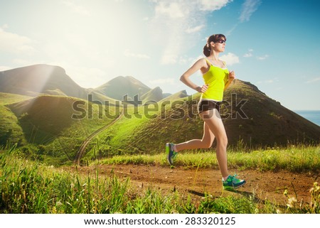 Running woman. Girl jogging on trail in mountains on field with grass in summer sunny day. Fitness. Healthy lifestyle.
