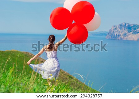 Happy woman with balloons into the field with green grass on the background of beautiful landscape. Celebration on nature outdoors.