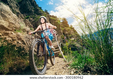 Happy woman cyclist rides in the mountains on a mountain bike. Portrait of a smiling girl on a bicycle traveling. Adventure travel.