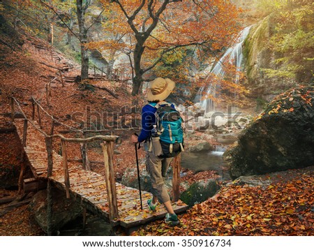 Woman backpacker walking on a wooden bridge over a river in the beautiful autumn forest. Hiking in the autumn forest trees.