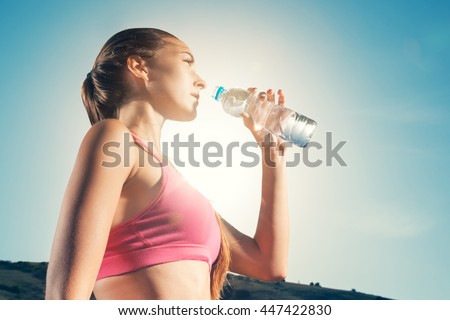 Young woman drinking water from plastic bottles after jogging. Girl quenches thirst after fitness outdoors. Lose weight. Healthy lifestyle.