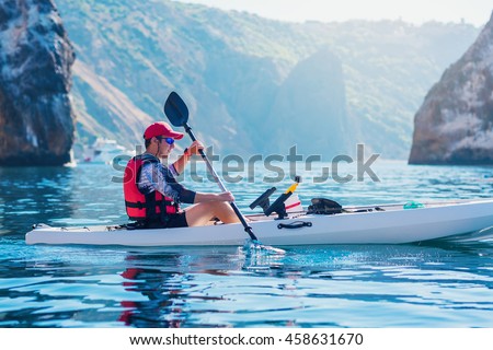 Kayaking. Man fisherman floats on a white kayak for fishing along the coast of the island near the rocks. Canoeing adventure on a calm sea with blue water.