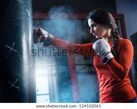 Young woman training punch boxing gloves for punching bag. Girl making Strong kick. CrossFit.