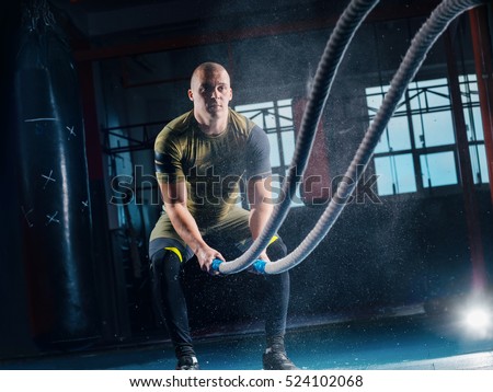 Men with battle rope battle ropes exercise in the fitness gym. CrossFit.
