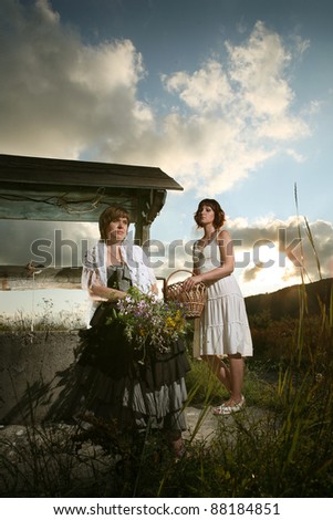 rural young women with a bouquet of wild flowers and a basket at the well