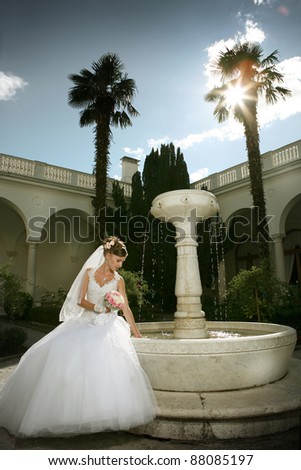 a beautiful young bride with a bouquet of flowers at the fountain in the wedding dress