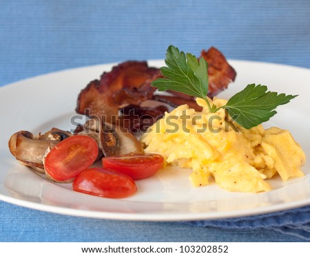 High protein breakfast. Egg and bacon. Lightly scrambled egg with grilled bacon, mushroom and tomato on blue linen.