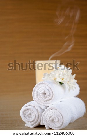 Simple fluffy white towels with flower and extinguished candle. Vertical image with copy space. Selective focus to emphasize soft towel texture.