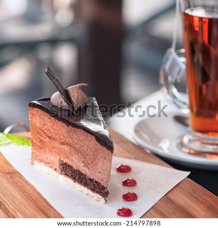 Slice of chocolate mousse cake served with glass of hot black tea in outdoor restaurant at afternoon tea time. Typical regional cuisine, Cape Province, South Africa. Selective focus, low key.