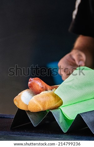Spicy, smoked sausage hotdog for sale, male street vendor's hand in background. Typical local street food, Prague, Czech Republic. Selective focus, low key lighting.