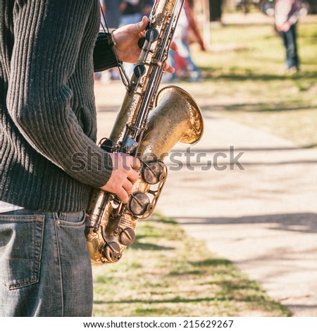 Solo Musician. Close up of Caucasian male hands holding battered old saxophone while playing jazz music in public park. Selective focus.