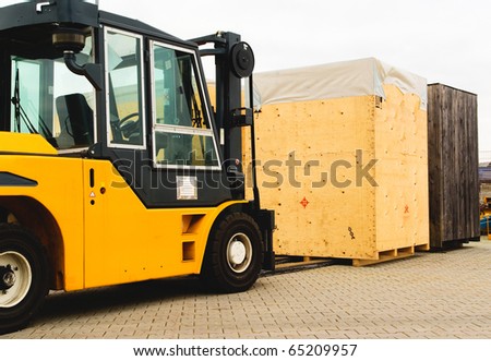 Forklift vehicle manipulating goods in logistic area outside warehouse.