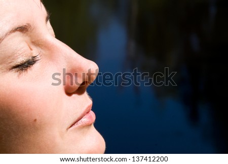 woman\'s face with closed eyes on a dark background in the sunlight in the profile
