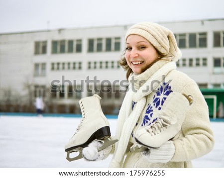 Positive girl with figure skates on the background of outdoor skating rink