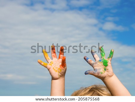 Hands of baby bedaubed with paint against blue sky
