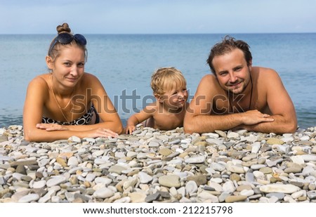 Young positive family from three persons lies on beach at the sea