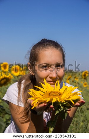 Young woman with sunflower in field against bright blue sky
