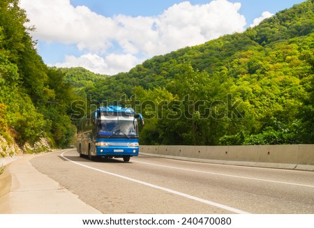 Dark blue tourist bus goes on road among mountains