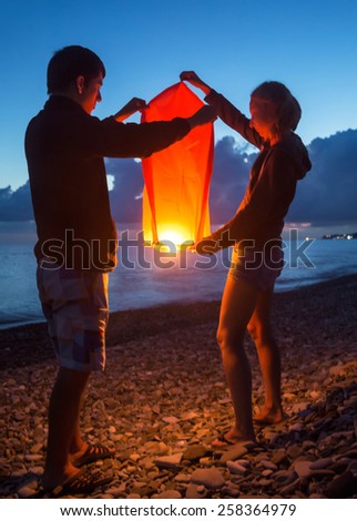Girl and young man start Chinese small lamp at the sea at night