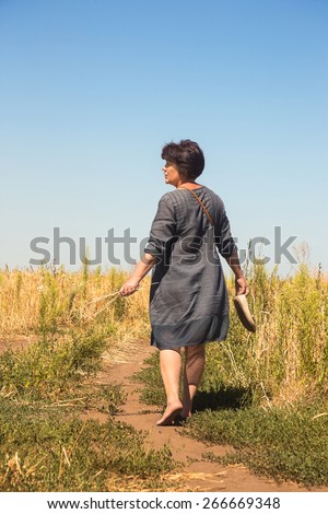 Barefooted woman leaves on path through field