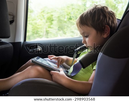 Little boy playing with concentration on computer tablet goes child seat in the car