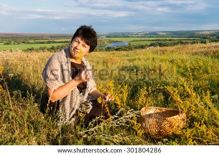 Positive fifty year old woman collects grass on meadow against the river