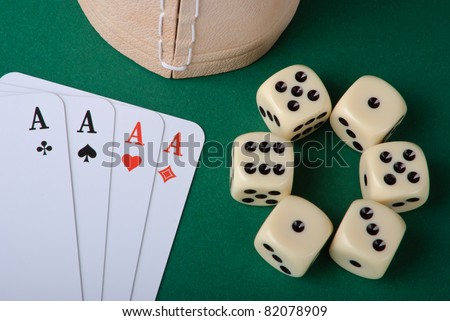 Four aces and six dices with cup on green background
