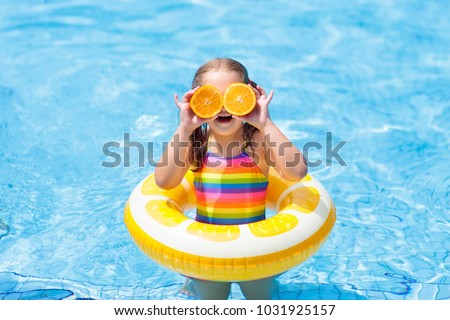 Little girl in swimming pool with inflatable toy ring eating orange. Kids swim on summer vacation. Tropical fruit and healthy snack. Swim aids for child.  Kid on colorful float. Beach and water fun.