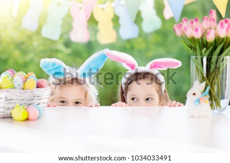 Family Easter morning. Children dye eggs. Kids with bunny ears search for candy and chocolate eggs on Easter egg hunt. Home decoration with tulip flowers, pastel rabbit banner and dye egg basket.