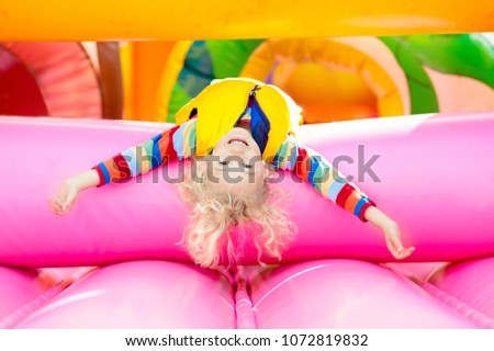 Child jumping on colorful playground trampoline. Kids jump in inflatable bounce castle on kindergarten birthday party Activity and play center for young child. Little boy playing outdoors in summer.
