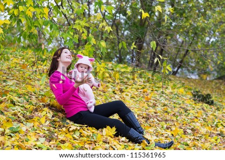 Attractive young mother holding a baby girl playing with falling autumn leaves