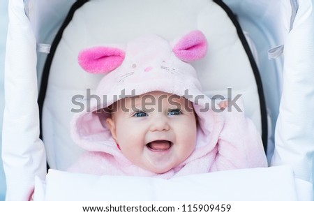 Sweet smiling baby girl in a bunny hat sitting in a white stroller