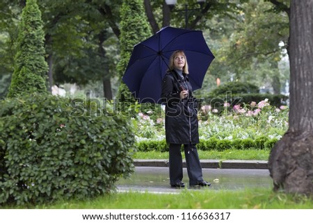 Elegant lady walking in a beautiful park under umbrella on a cold rainy day