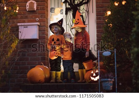 Halloween trick or treat. Children in black and orange witch costume and hat standing at house door with pumpkin and spider decoration. Kids trick or treating. Boy and girl with candy buckets.