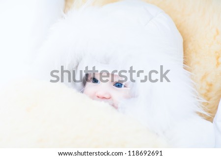 Baby girl in a white fur jacket sitting in a stroller with a warm sheepskin foot muff