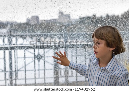 Cute boy standing next to a wet window on a rainy day