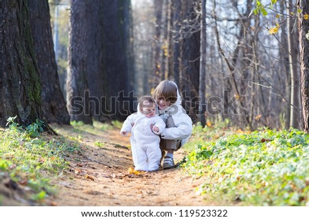 Boy playing with his baby sister in the park on a cold day