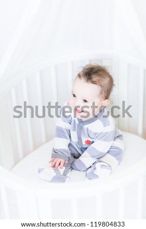 Sweet baby girl sitting in a round white bassinet