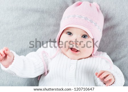 Sweet baby girl on a grey blanket wearing a pink hat