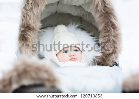 Sweet little baby sitting in a winter fur stroller on a snowy day