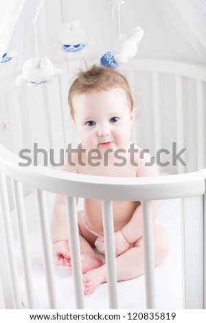 Very beautiful baby sitting in a white round crib