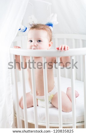 Funny baby sitting in a round white crib