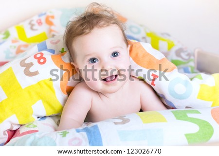 Funny little baby playing peek-a-boo under a colorful blanket