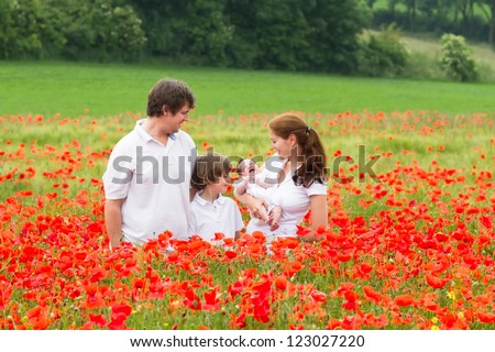 Happy young family with a son and a newborn daughter standing in a beautiful poppy flower field