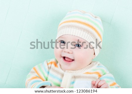 Cute little baby in a knitted jacket and hat on a green blanket