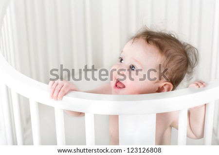 Funny little baby standing in a white round crib