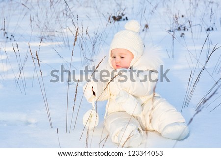 Funny baby playing with grass in a snow field on a sunny day