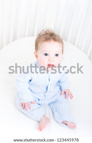 Funny baby sitting in a white round crib