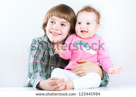 Brother hugging his baby sister, both wearing green and pink shirts